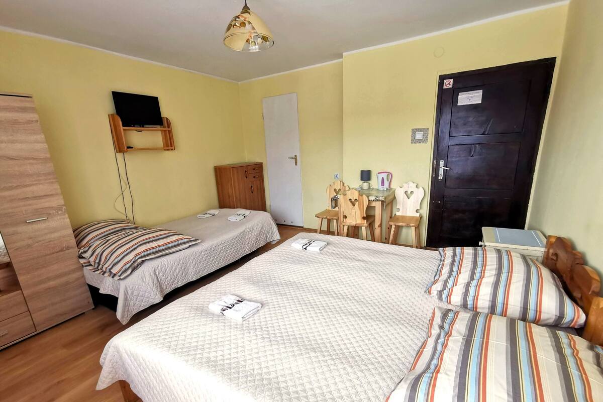 Ein Zimmer mit zwei Betten, einem Holzschrank, einem Schreibtisch mit Stuhl, einer Lampe und einer Tür mit einem Schild.