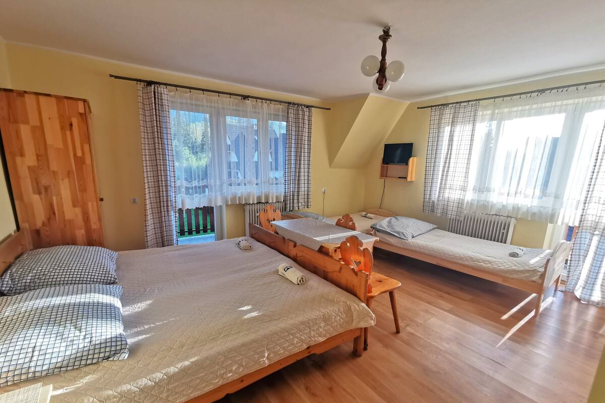 Ein Zimmer mit zwei Holzbetten, einer Holzbank, einem Deckenventilator und einem Fenster mit Vorhängen.