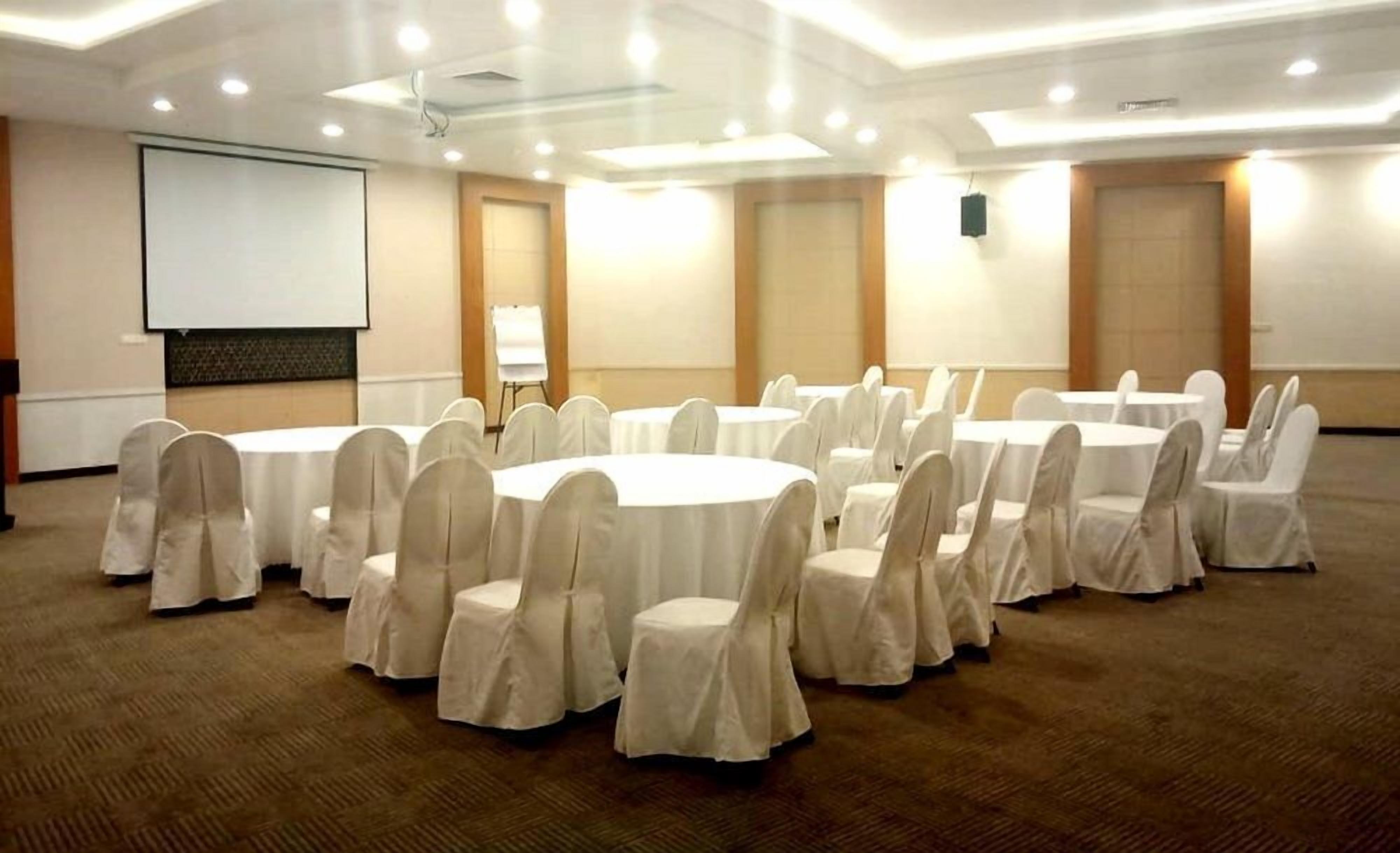 A conference room with round tables and chairs, a projector screen, and a whiteboard.