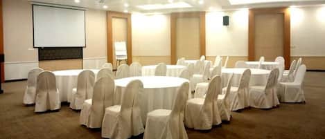 A conference room with round tables and chairs, a projector screen, and a whiteboard.