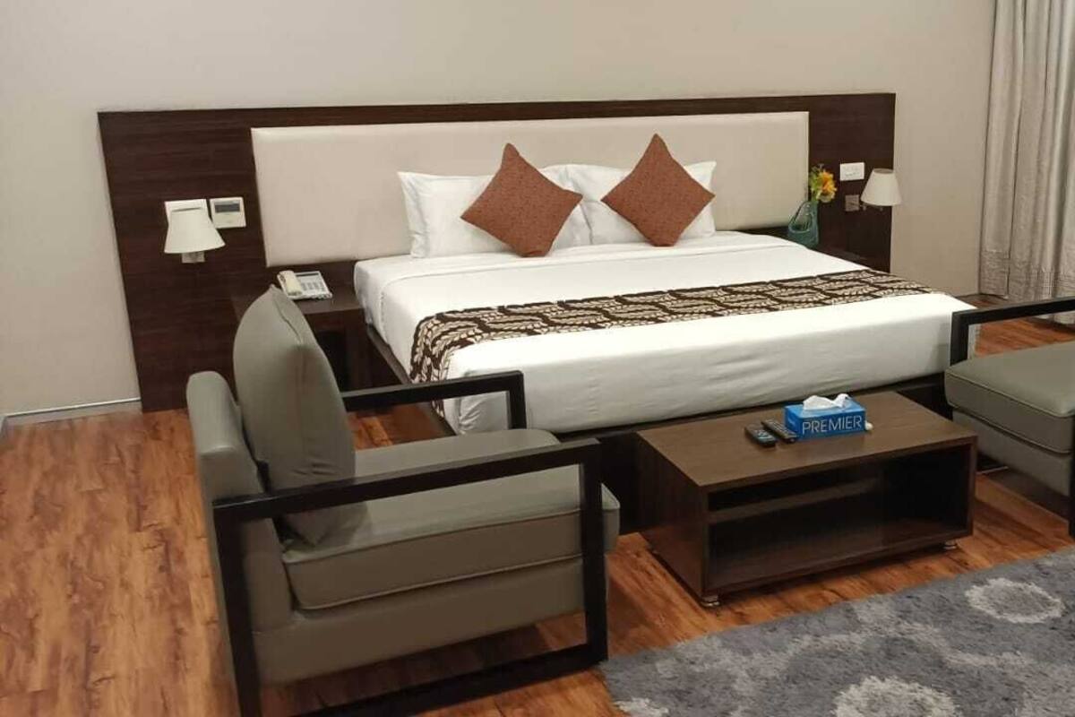 A hotel room with a bed, two armchairs, a coffee table, and a small table with a lamp and phone.