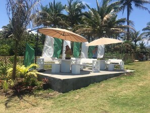 A stage with white furniture and green curtains, surrounded by palm trees. - Pacific Buddies - Campsite (Dingalan)