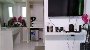A compact hotel room with a bed, a small desk with a mirror, a television mounted on the wall, and a shelf with decorative items. - Pacific Buddies - Campsite (Dingalan)