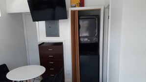 Quarto compacto com cama, uma mesinha, TV fixada na parede e forno embutido.