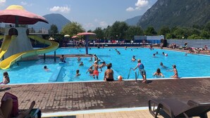 En swimmingpool med vandrutsjebaner og parasoller, omgivet af bjerge.