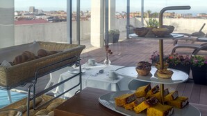 Eine Dachterrasse mit einem Buffet aus Gebäck und Desserts, einem Korbwägelchen und Blick auf die Stadt.