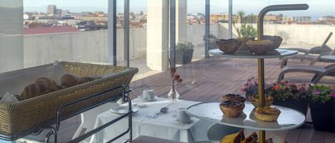 A rooftop terrace with a buffet of pastries and desserts, a wicker basket, and a view of the cityscape.
