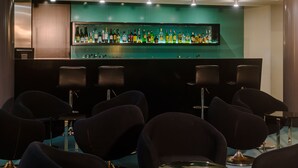 Eine Bar mit einer Glasvitrine voller Flaschen, schwarzen Barhocker und einer wandfarben in Türkis.