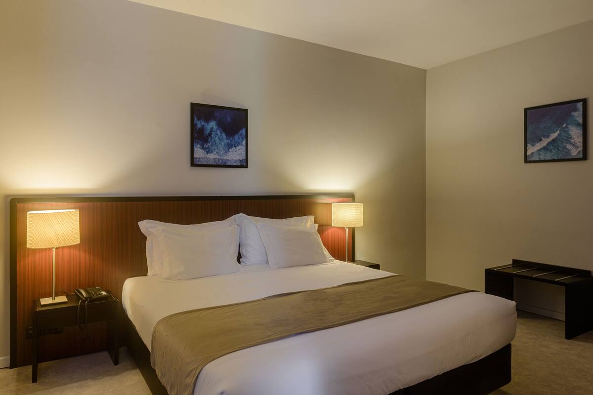 A hotel room with a large bed, two bedside lamps, a nightstand with a phone, and two framed pictures on the walls.