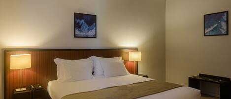 A hotel room with a large bed, two bedside lamps, a nightstand with a phone, and two framed pictures on the walls.