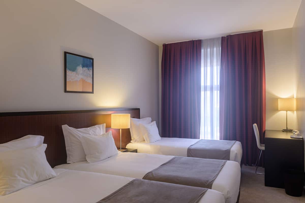 A hotel room with two beds, a desk, a chair, a lamp, and a painting on the wall.