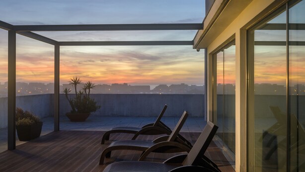 Eine Dachterrasse mit Sonnenuntergangsblick, Holzboden und Liegestühlen.