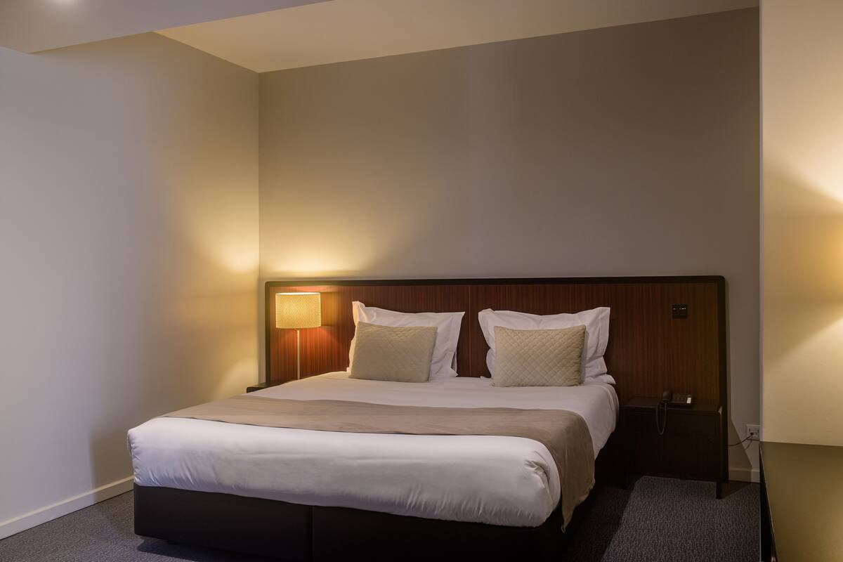 A neatly made bed with a wooden headboard, a bedside lamp, and a small nightstand.