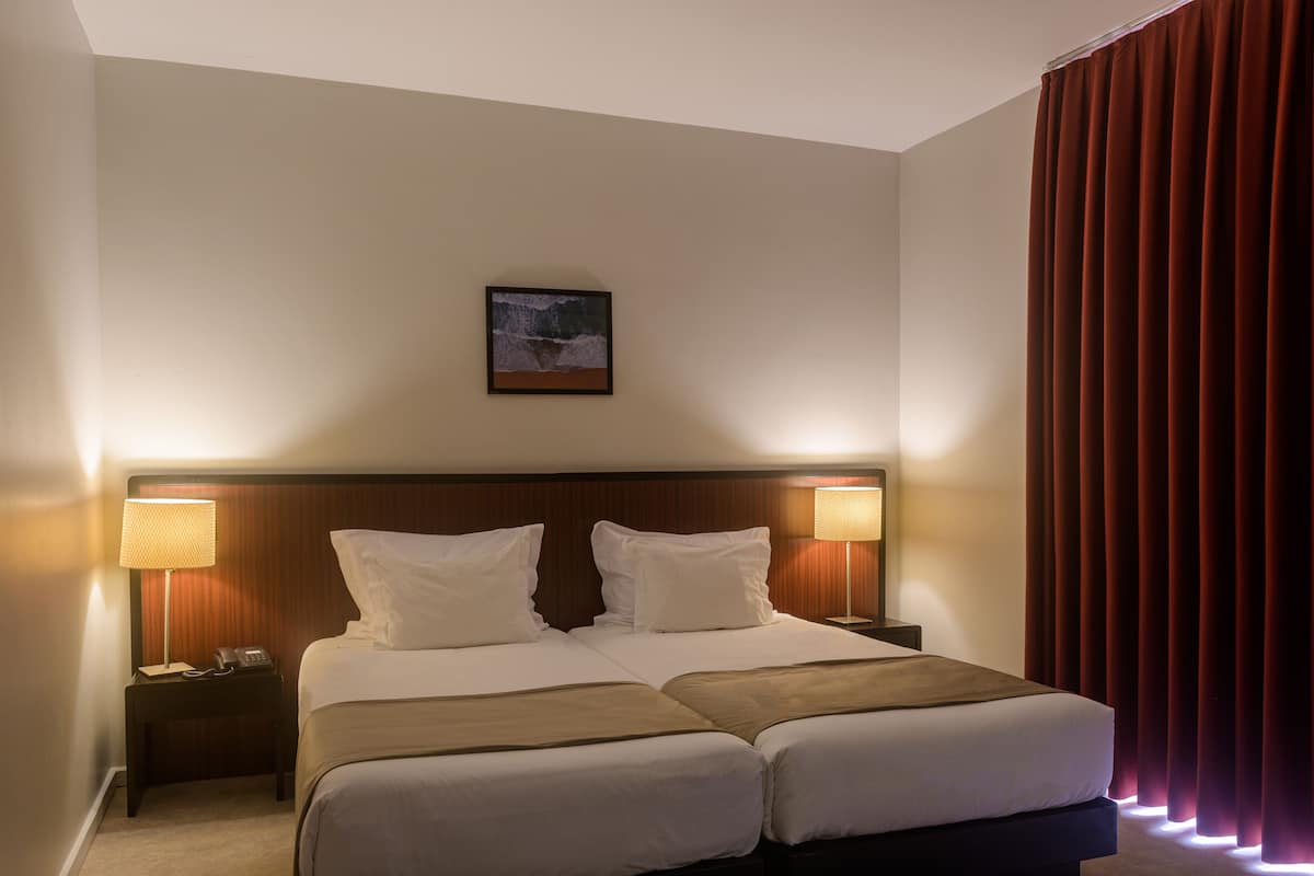 A hotel room with two beds, a headboard, bedside lamps, a nightstand, and a framed picture on the wall.
