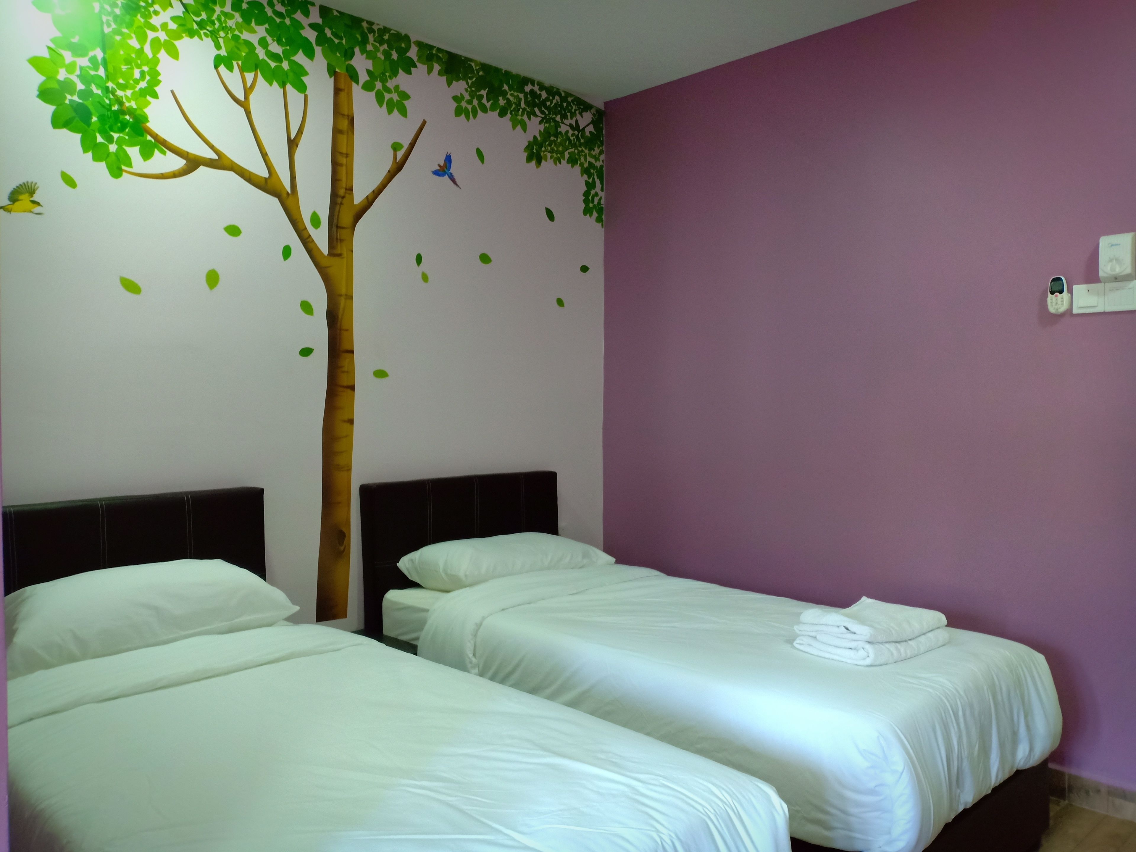 A hotel room with two beds, a tree decal on the wall, and a purple accent wall.