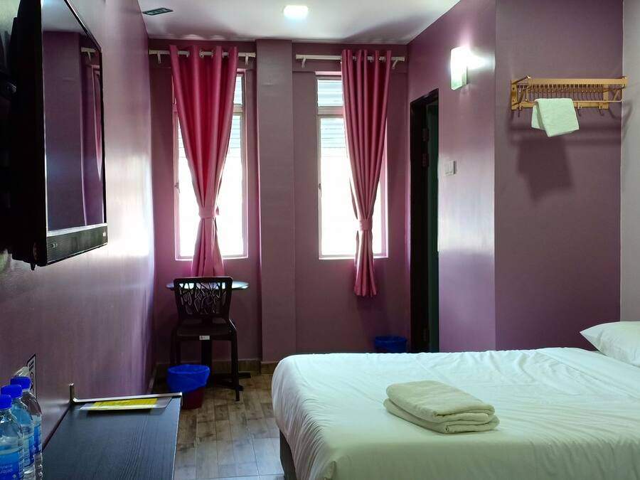 A hotel room with a bed, a TV mounted on the wall, a chair, and a table with water bottles.