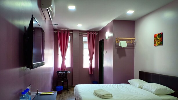 A hotel room with two beds, a desk, a TV, and a window with curtains.