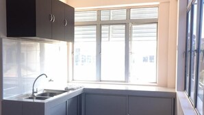 A compact kitchen with a window, dark tiles, and grey cabinets.