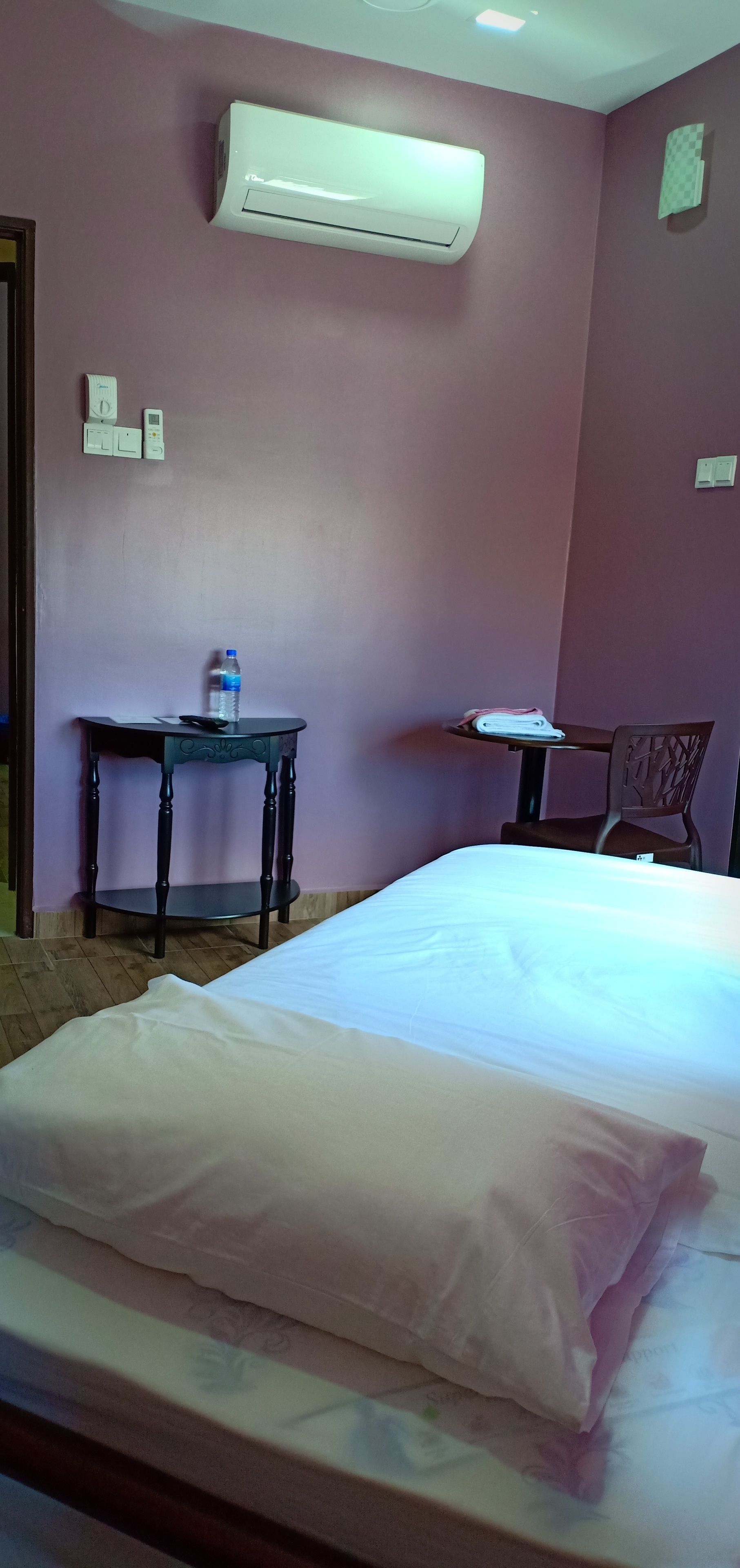 A room with a bed, a table with a water bottle, and an air conditioning unit on the wall.