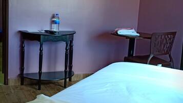A room with a bed, a table with a water bottle, and an air conditioning unit on the wall.