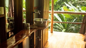 Un baño con tocador de madera, un lavamanos de acero inoxidable y una ventana con vistas a la vegetación.