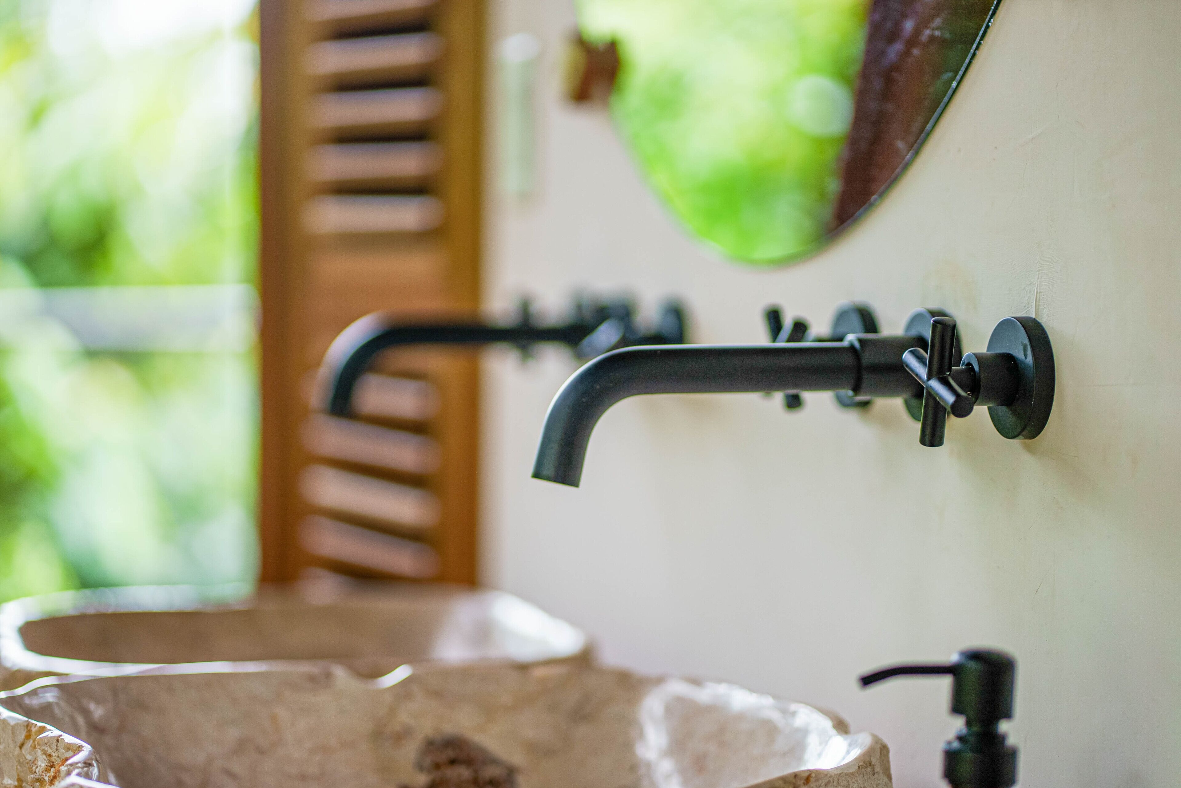 Un baño con un lavamanos de piedra, un grifo negro y un espejo verde.