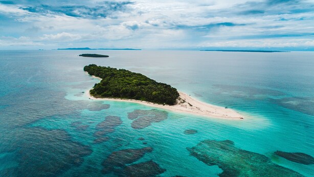 Vista aérea de una isla tropical con aguas turquesas cristalinas, una playa de arena y abundante vegetación.