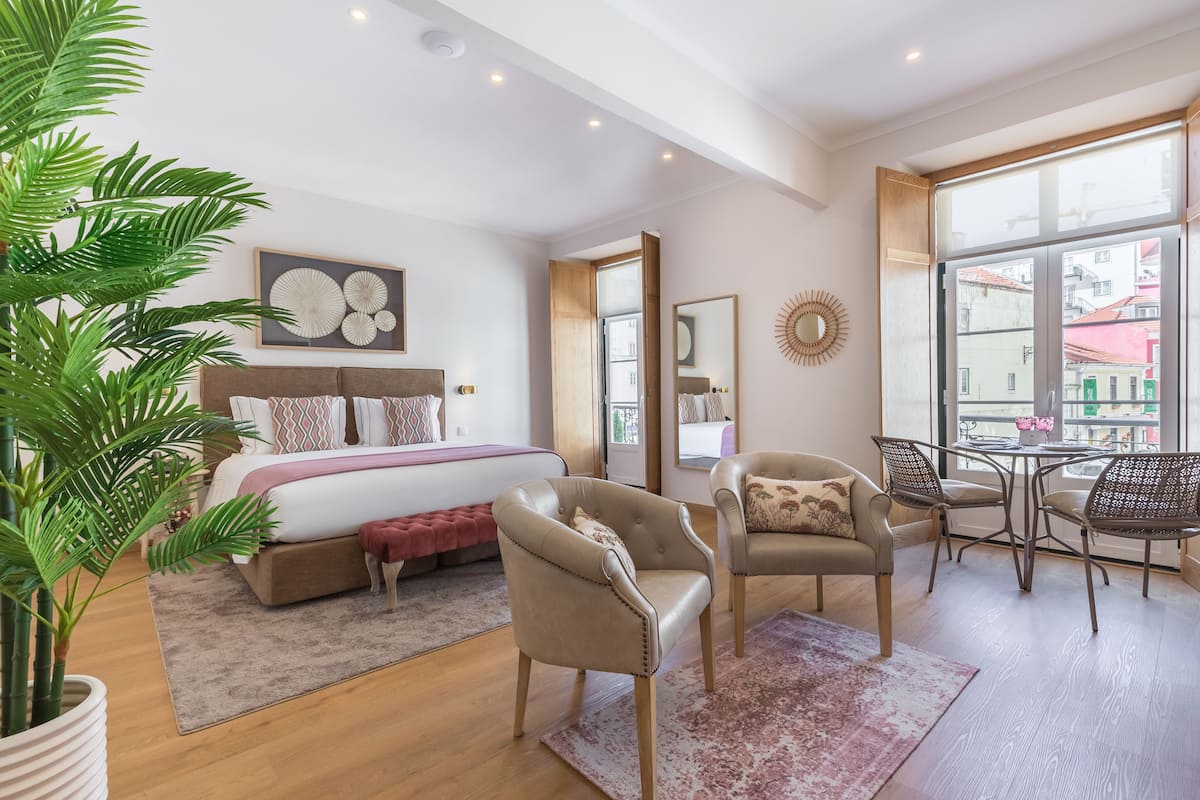 Un dormitorio moderno con una cama grande, un espacio de descanso con sillas, una mesa de comedor y un ventanal con vista a la ciudad.