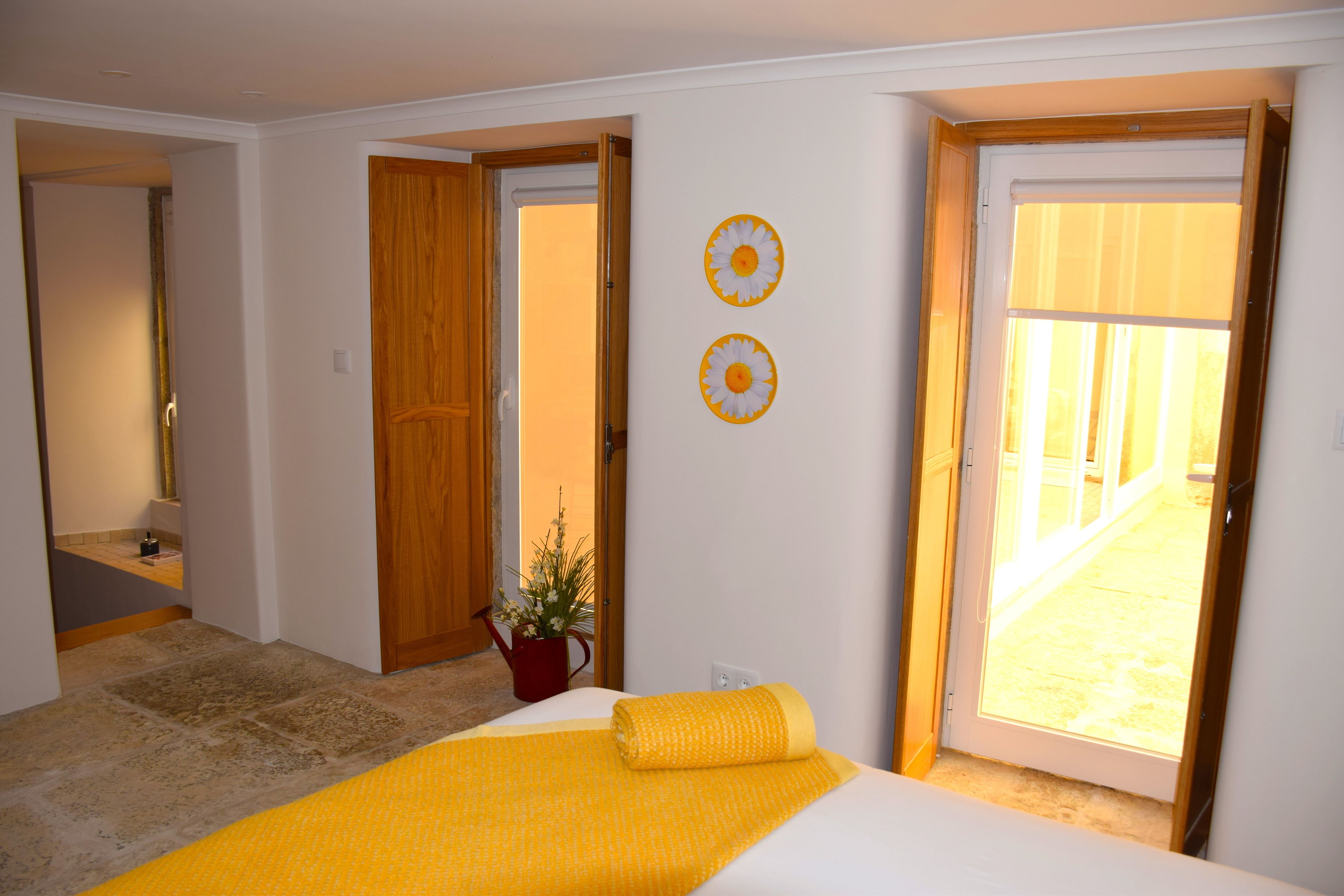 Ein Schlafzimmer mit einem Bett, einer Holztür, einem Topfpflanzen und Blick durch eine Glastür.