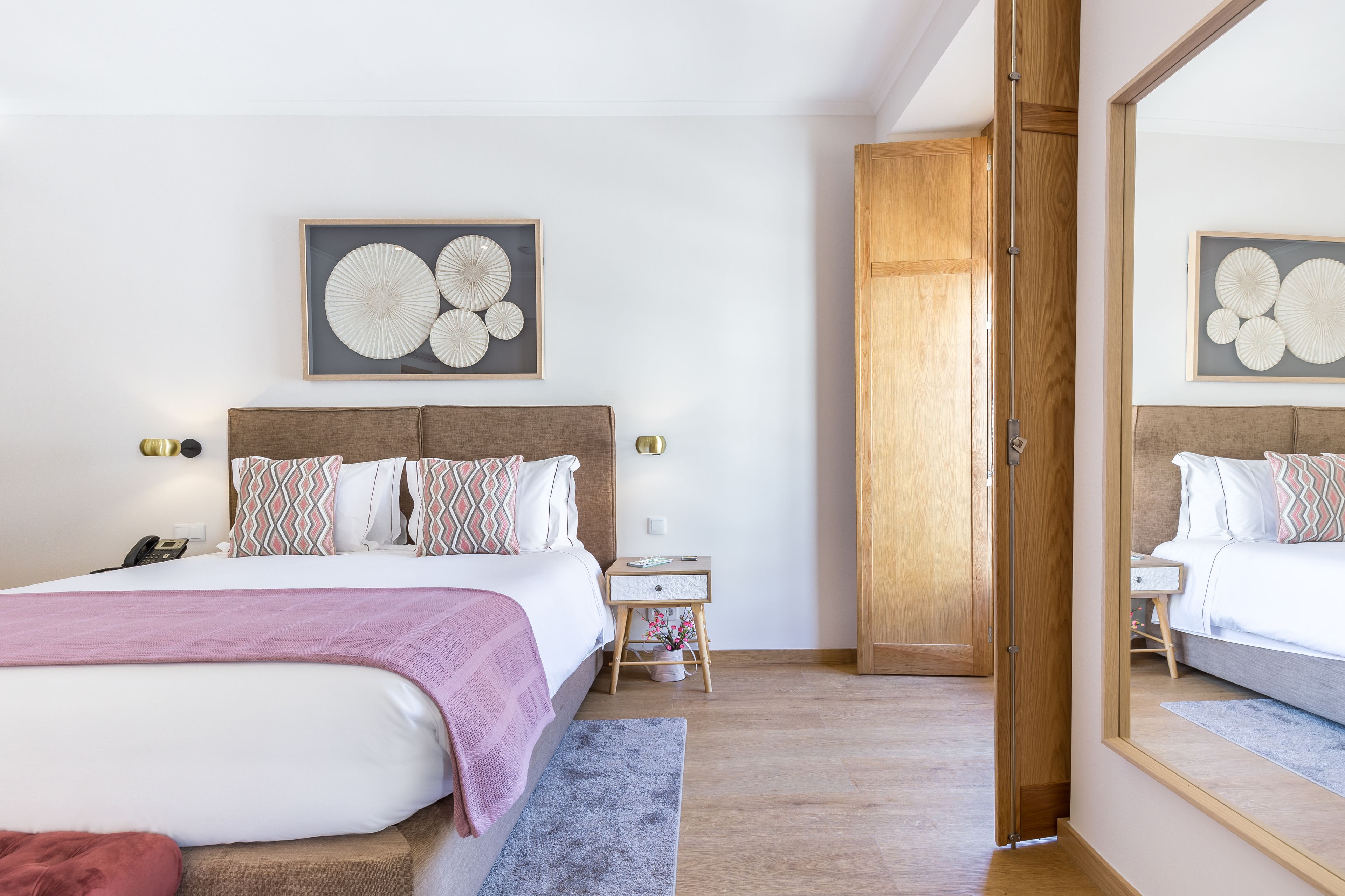 A bedroom with a large bed, bedside tables, a mirror, and artwork on the wall.