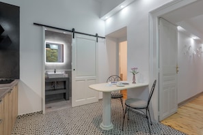 Une salle de bain moderne avec une douche, un lavabo et un meuble-lavabo. On y trouve une table avec une chaise et un vase rempli de fleurs.
