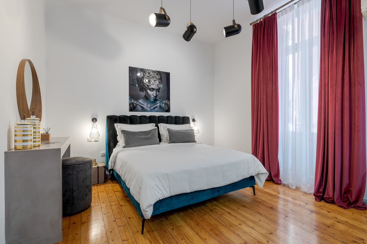 A modern bedroom with a large bed, a bedside table, a mirror, and a wall-mounted artwork.