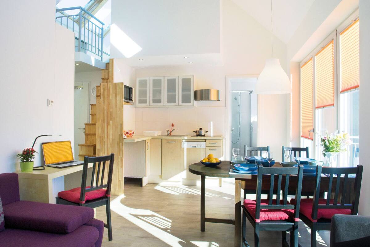 A modern apartment with a dining area, kitchen, and a staircase leading to an upper level.