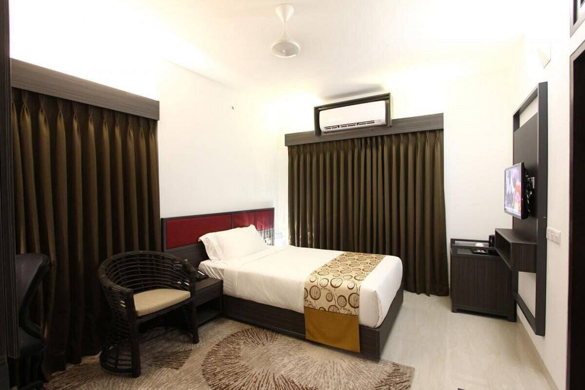 Une chambre d’hôtel avec un lit, une chaise, un bureau, une télévision et une fenêtre avec des rideaux.