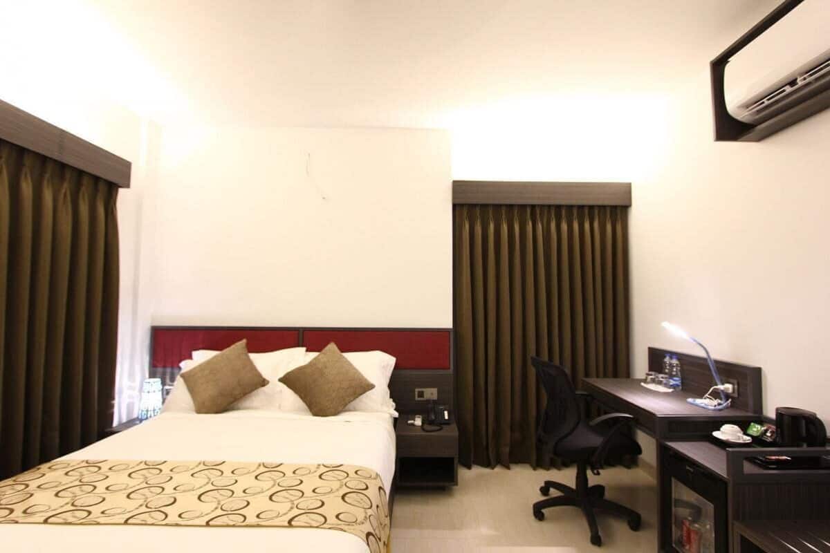 Une chambre d’hôtel équipée d’un lit, d’un bureau, d’une chaise, d’une table de chevet et d’un climatiseur fixé au mur.