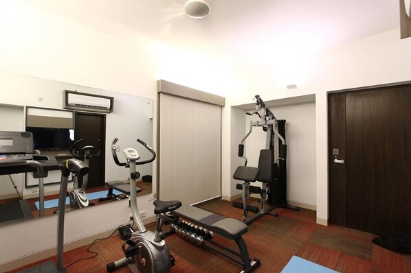 A hotel room with a treadmill, elliptical, and weight bench.