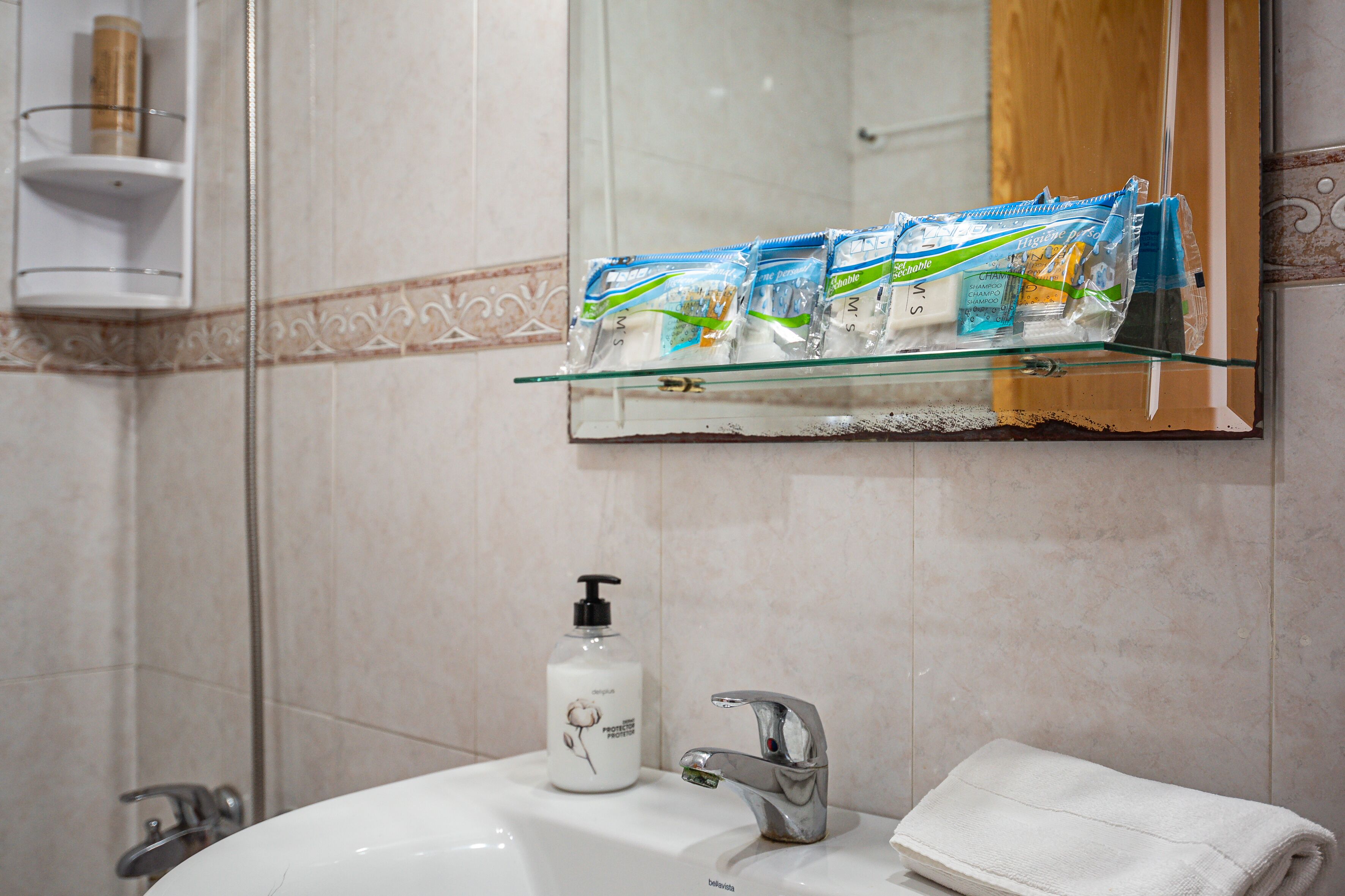 Une salle de bain avec une étagère en verre où sont rangés les articles de toilette, un lavabo avec un robinet et un miroir au-dessus du lavabo.