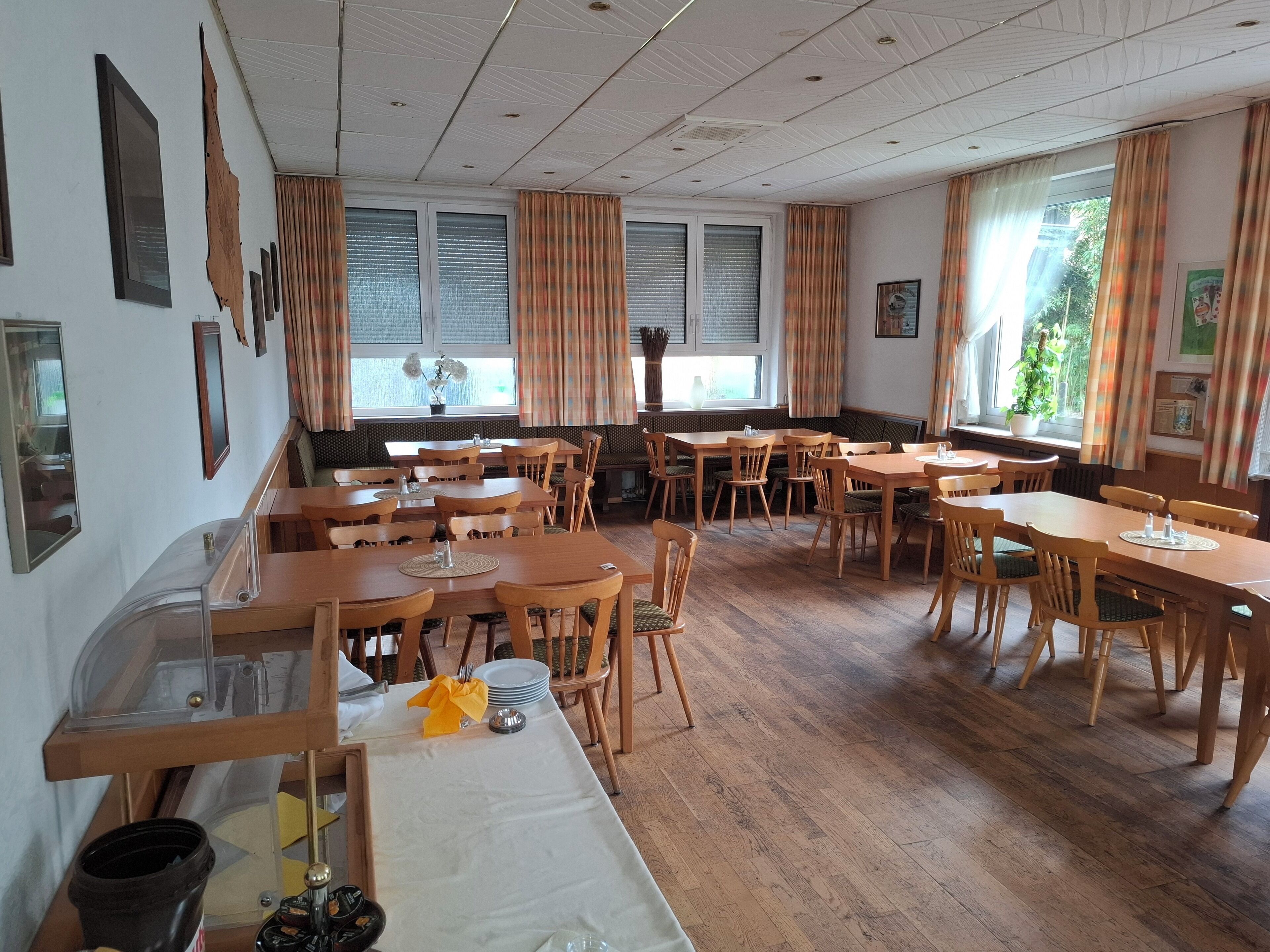 Un comedor con mesas y sillas de madera, una barra larga y un ventanal con cortinas.