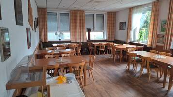 Un comedor con mesas y sillas de madera, una barra larga y un ventanal con cortinas.