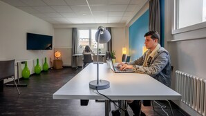 A modern office space with a long table, a desk lamp, and a laptop. - Nyon Hostel (Nyon)