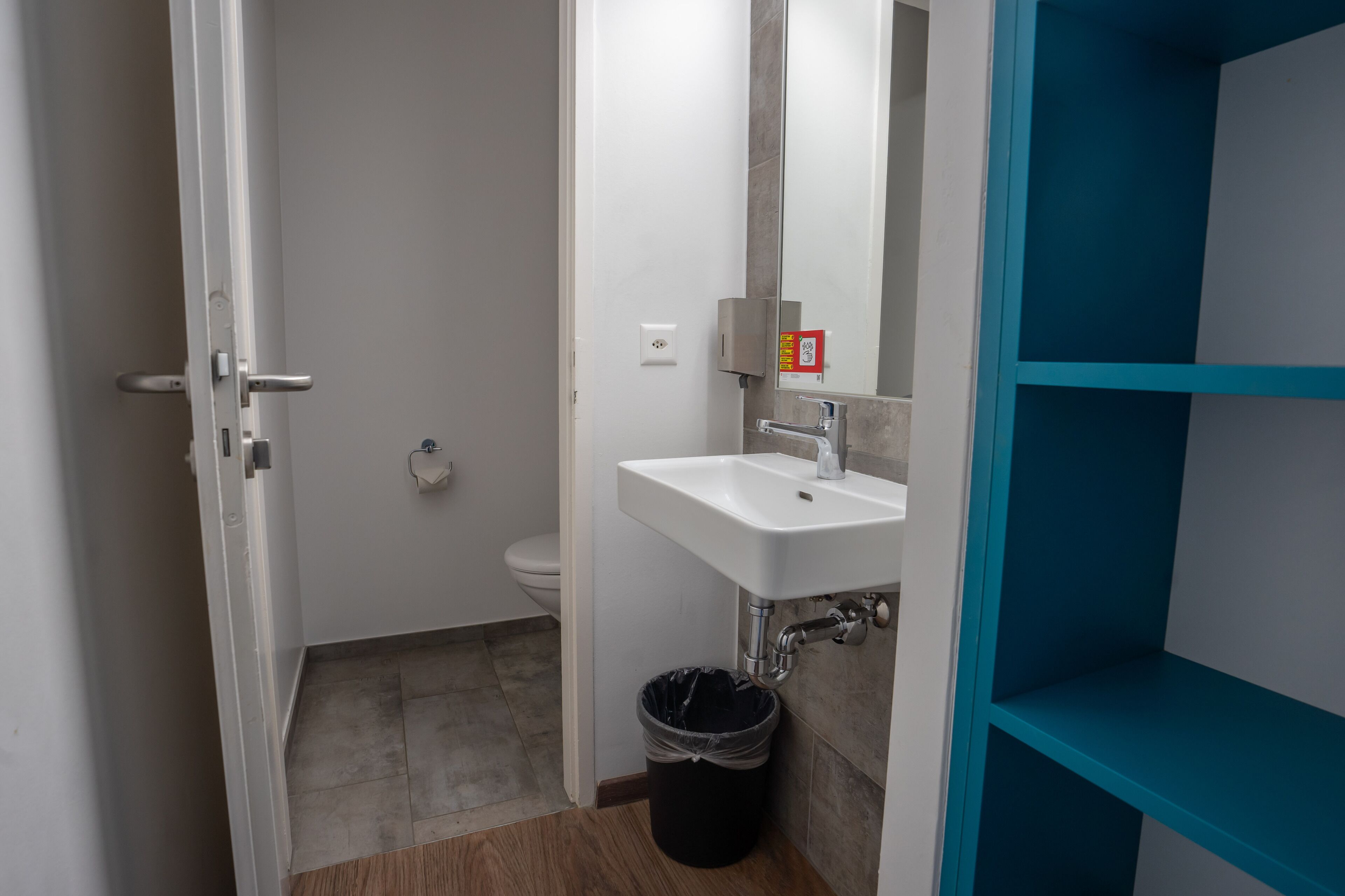 Un baño con un lavamanos blanco, un espejo y un estante azul.