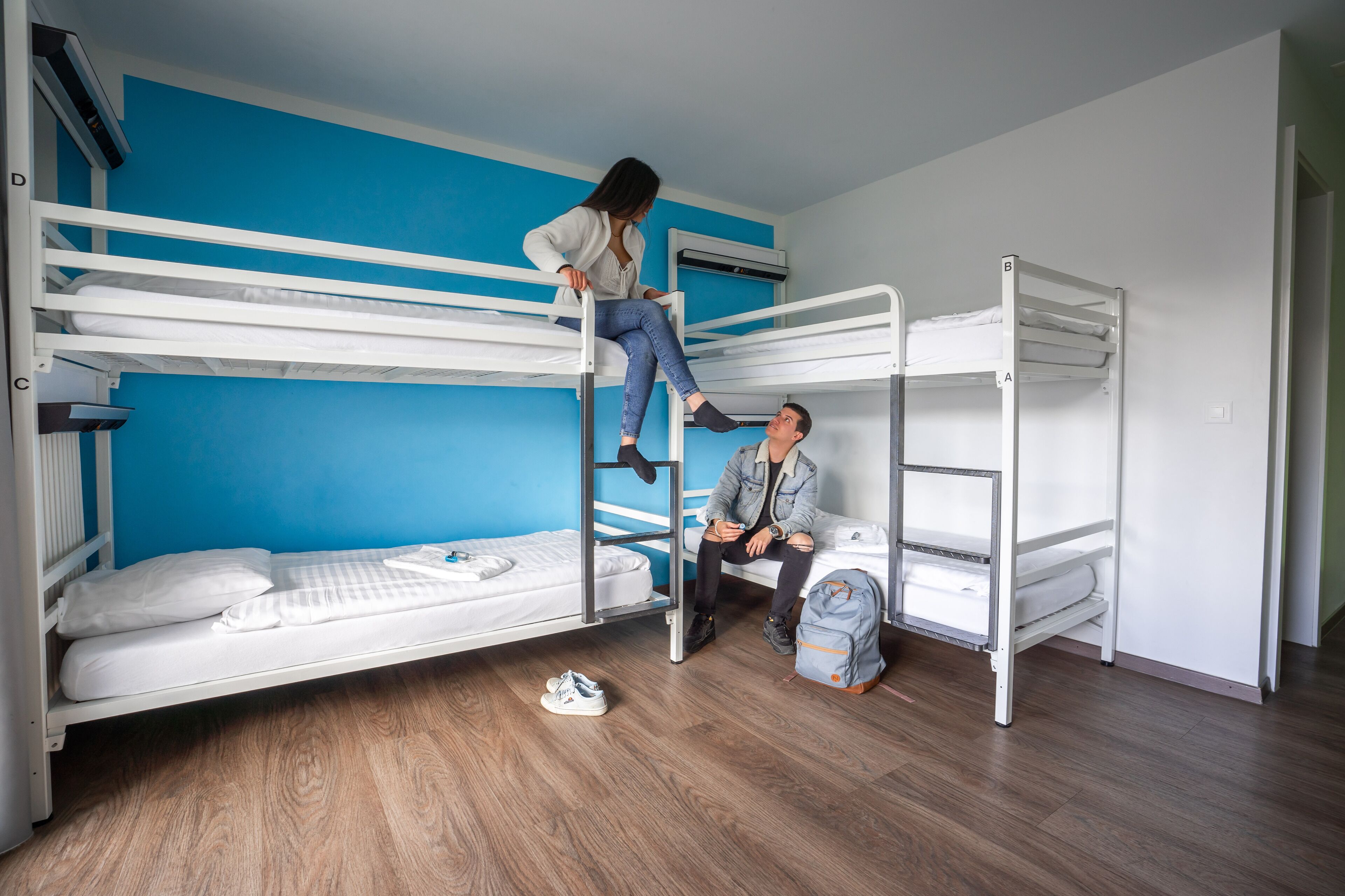 Habitación con literas, pared azul, suelo de madera y unidad de aire acondicionado blanca.