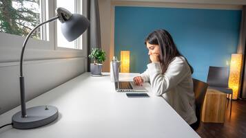 Una persona trabajando en un escritorio con una computadora portátil, una lámpara y una planta en maceta.
