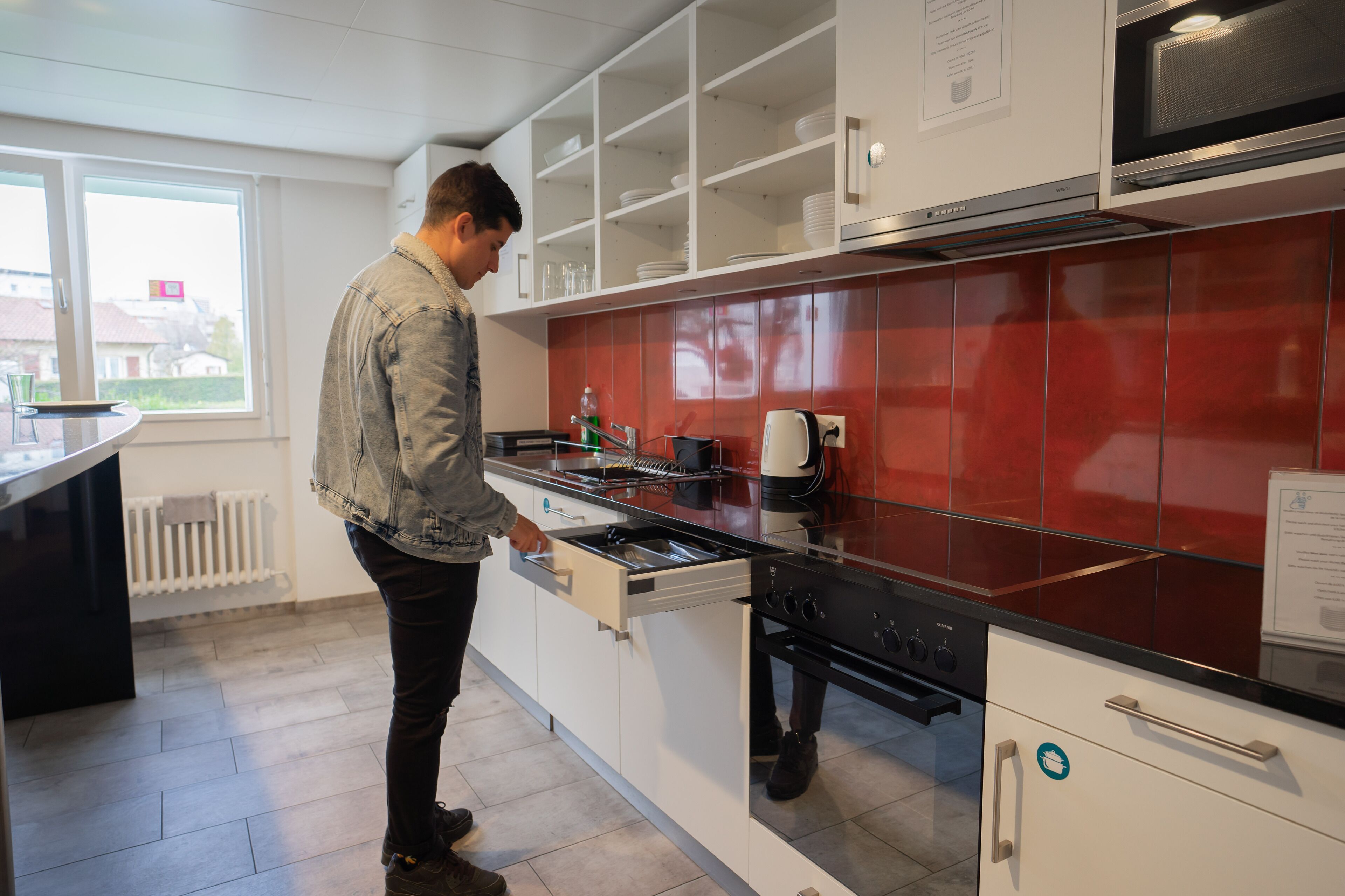 Una cocina moderna con armarios blancos, salpicadero rojo y electrodomésticos de acero inoxidable.