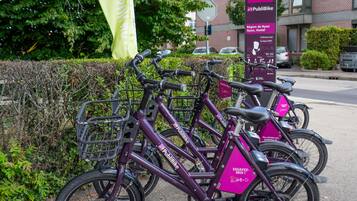 Una fila de bicicletas moradas estacionadas frente a un edificio con un cartel que dice 'Public Bike' y 'Région de Nyon, Nyon Hostel'.