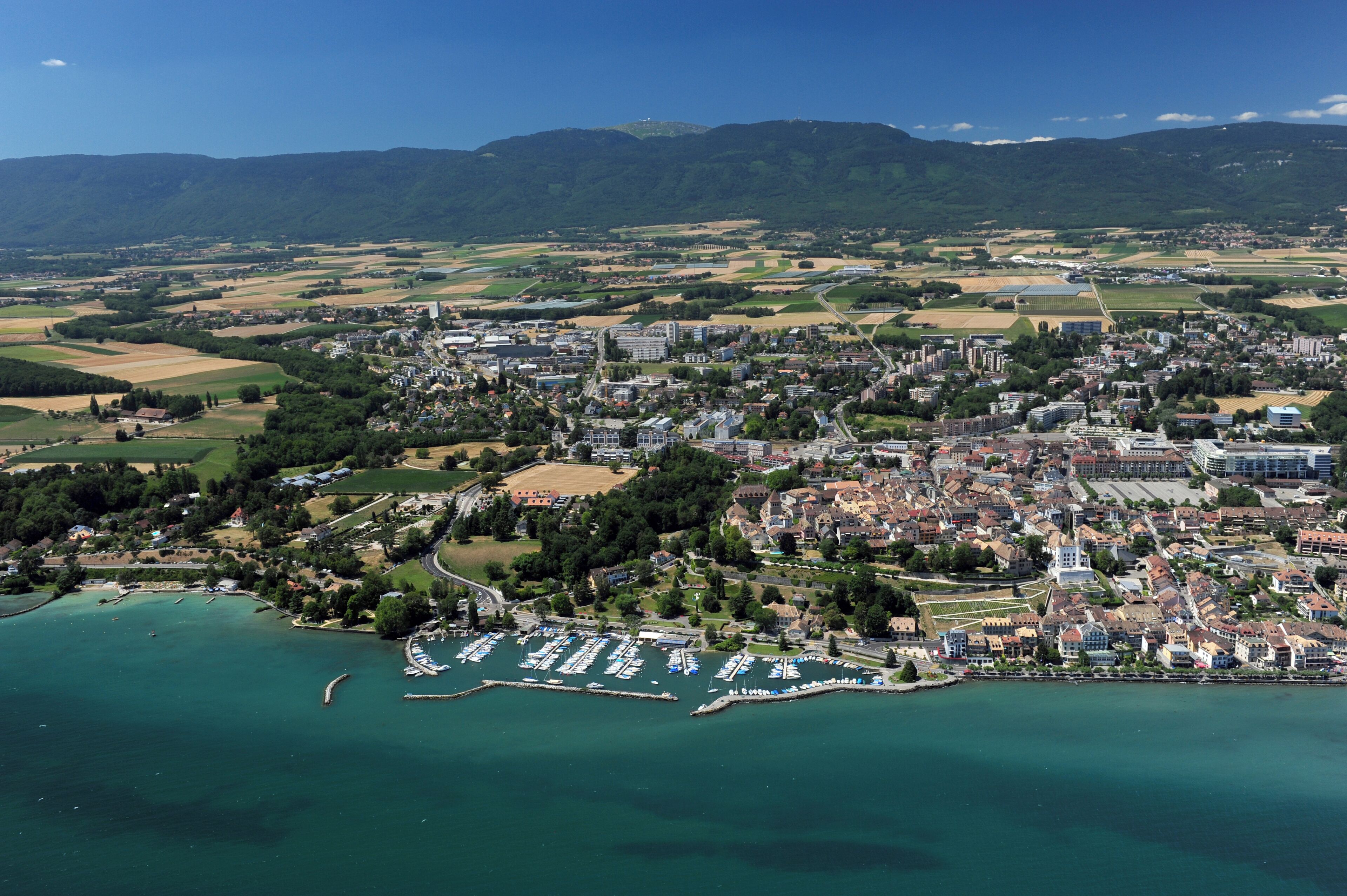 Vue aérienne d’une ville côtière avec un port de plaisance, des zones résidentielles et des champs environnants.