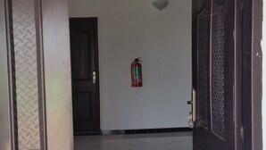 An interior hallway with a fire extinguisher mounted on the wall, a door with a textured pattern, and a tiled floor. - Mac-P Guesthouse (Kweiman)