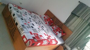 A bed with a patterned bedspread, a wooden headboard, and a window with curtains. - Mac-P Guesthouse (Kweiman)
