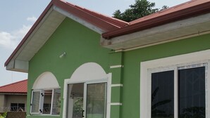 A green house with a red roof, white-framed windows, and a tiled entrance. - Mac-P Guesthouse (Kweiman)