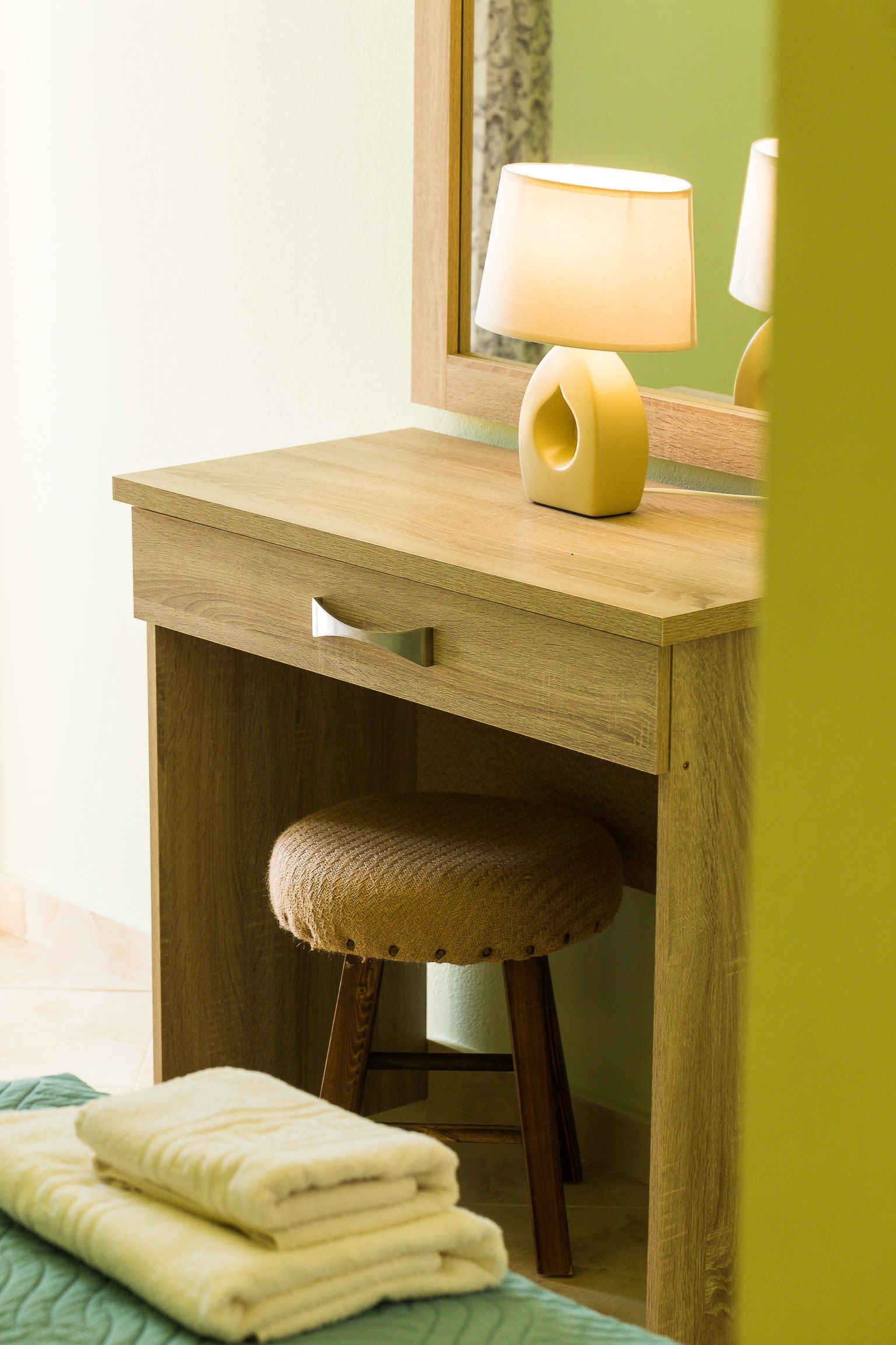 Een houten bureau met een lamp, een comfortabele kruk en opgevouwen handdoeken.